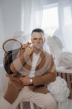 Stylish male embodies the old-money look, posing with a bag and tennis racket