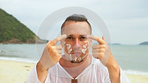 Stylish man on beach near sea smearing sunscreen cream in style war paint.Close-up portrait man apply sun cream