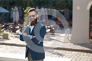 Stylish man with beard on the sunny street with crossed hands on his chest