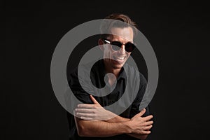 Stylish man a black shirt and sun glasses isolated over black background. Low key portrait.