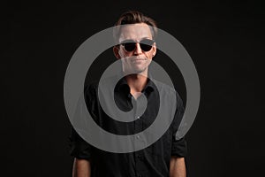 Stylish man a black shirt and sun glasses isolated over black background. Low key portrait.