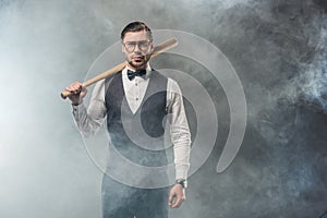 stylish man in bow tie and eyeglasses holding baseball bat and looking at camera