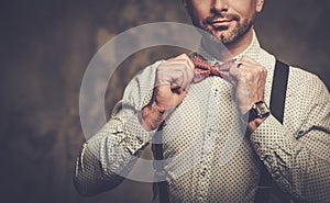 Stylish man with bow tie wearing suspenders and posing on dark background.