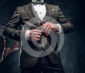 A stylish man buttoning his elegant jacket against a dark textured wall