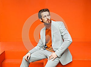 Stylish man in a fashionable suit sits against the background of an orange wall