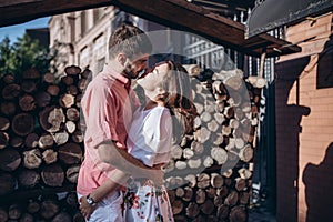 Stylish man and happy woman embrace in light on background of wooden firewood wall. Happy couple are hagging, romantic moment.