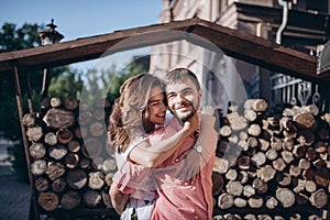 Stylish man and happy woman embrace in light on background of wooden firewood wall. Happy couple are hagging, romantic moment