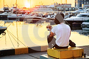 Stylish man and his dog sitting together on pier and enjoying colorful sunset.