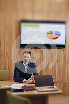 A stylish man in a jacket and shirt sits at the desk with his colleagues and works with documents at office