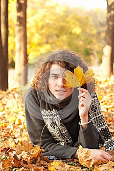 Man in knit sweater and scarf lying on autumn leaves, oudoor in autumn park. photo