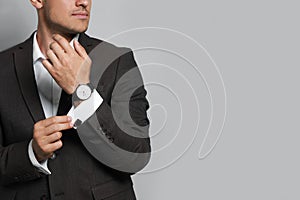 Stylish man putting on cufflink against grey background, closeup. Space for text