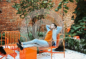 A stylish man rests and relaxes with his hands behind his head on a summer day in the city.