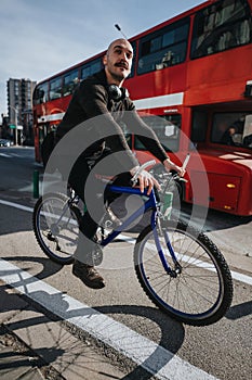 Stylish man riding a bike on the city street with red bus in the background.