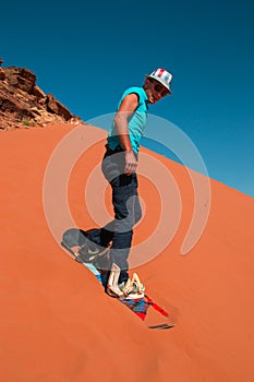 Stylish man sand boarding in desert down red dune Wadi Rum Jordan. Active rest, travel, healthy lifestyle concept.