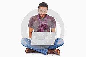 Stylish man sitting on floor using laptop and smiling at camera