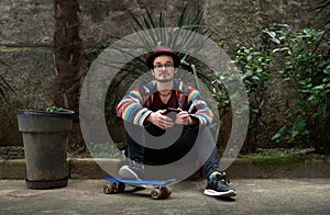 Stylish Man Sitting with Smartphone and Skateboard