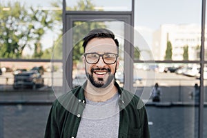 Stylish man smiling at camera and standing at office building