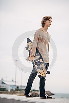 Stylish man stands on street and hold long board in hands