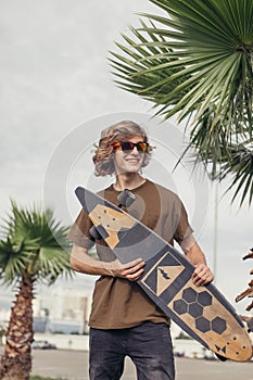 Stylish man stands on street and hold long board in hands