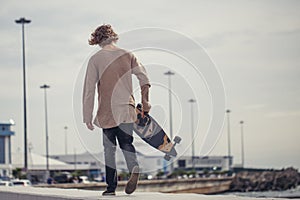 Stylish man stands on street and hold long board in hands