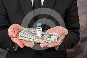 Stylish man with strong hands in a suit carries the vaccine in a jar and dollars for it.
