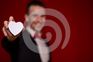 Stylish man in suit holding love gift box with red background, focus on gift box