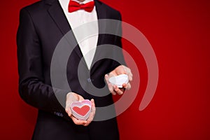 Stylish man in suit holding love gift box with red background, focus on gift box