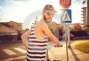 Stylish man in sunglasses riding a bicycle on a city street at s