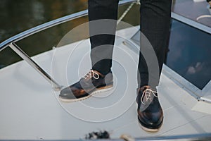 Stylish man in textured black suit pants and dark brogue shoes, standing on a boat