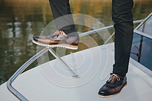 Stylish man in textured black suit pants and dark brogue shoes, standing on a boat