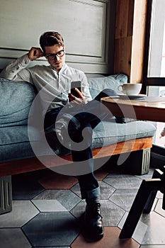 Stylish man using a smartphone, sitting on couch at cafe