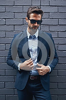 Stylish, man and wall in suit with sunglasses for fashion, style and trendy in outdoor. Male person, pride and