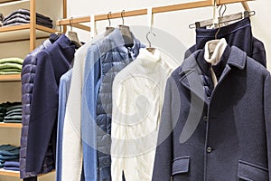 Stylish men`s clothing collection on hangers and shelves in the store. Sweaters, jackets and trousers