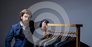 Stylish men's suit. workshop. Handsome bearded fashion man in classical costume suit. Male suits hanging in a row