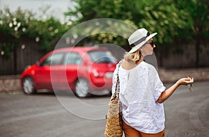 Stylish, mid-aged woman holding keys to new red car and looking at a car. Ready for car trip.