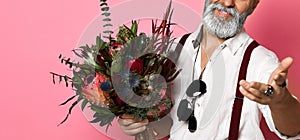 Stylish middle-aged bearded man with a modern haircut and fashionably dressed holds a bouquet of flowers.