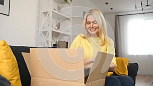 Stylish middle-aged blonde woman sitting on the couch with carton box on laps