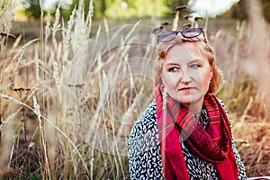 Stylish middle-aged woman chilling in autumn field. Senior lady wearing clothes and accessories. Harmony and balance