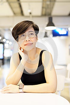 Stylish middle Asian woman smiling, sitting, looking up in modern cafe