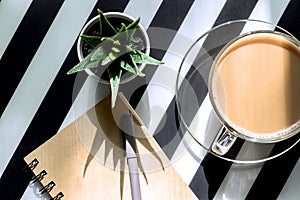 Stylish minimalistic workspace with  notebook, pen, cup of coffee and succulent on striped black and white background. Flat lay