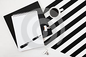 Minimalistic workspace with book, notebook, pencil, cup of coffee on striped black and white background. Flat lay style Top view