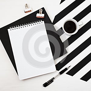 Minimalistic workspace with book, notebook, pencil, cup of coffee on striped black and white background. Flat lay style Top view