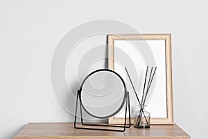 Stylish mirror, reed diffuser and picture frame on table near light wall