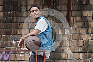 stylish mixed race man standing with basketball ball and looking away