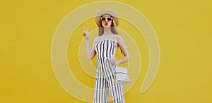 Stylish model woman wearing summer round straw hat, white striped jumpsuit posing on an yellow background