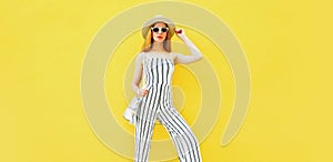 Stylish model woman wearing summer round straw hat, white striped jumpsuit posing on yellow background