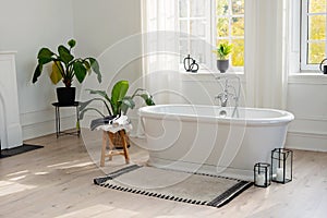 Stylish modern bathroom interior. Horizontal view of an empty free-standing bathtub on a wooden floor in a bright room against the