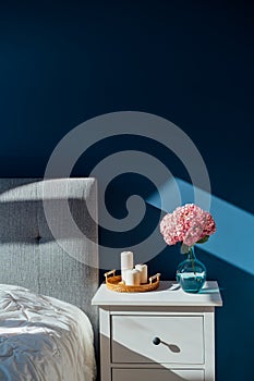 Stylish modern bedroom in dark colors. Cozy interior with navy blue walls, home decor. Bed with grey fabric headboard