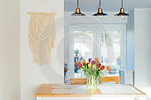 Stylish and modern boho, scandi interior of open space white kitchen with tulip flowers in vase on the wooden kitchen