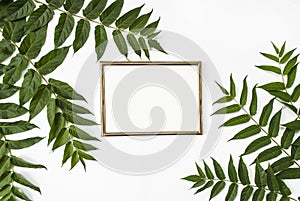 Stylish modern composition. Golden empty frame and green tropical leaves on a white background. Flat lay. Mock up